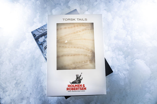 Boks med torsk tails med Holmen & Robertsen-logo som ligger på is.
